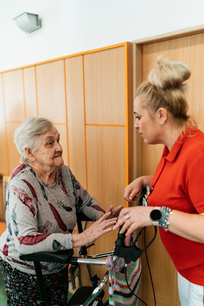 our-story A caregiver assists an elderly woman in a retirement home corridor, fostering companionship and support.