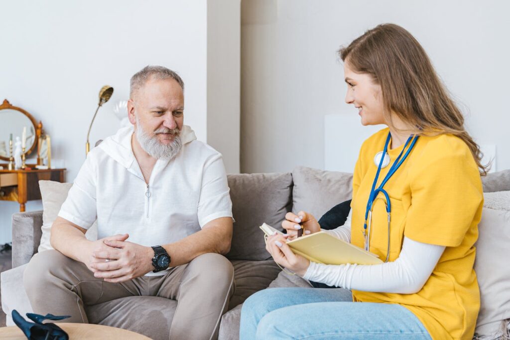 pexels-photo-7345460 A healthcare professional smiles while consulting with an elderly man in a cozy indoor setting.