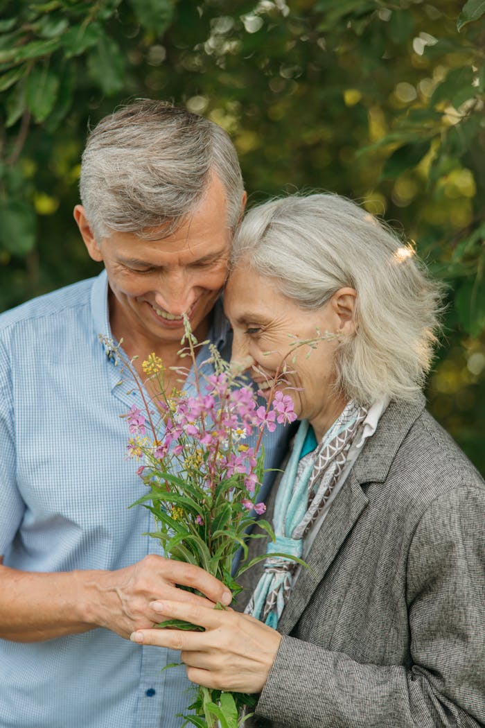 who-we-are An elderly couple shares a joyful moment embracing flowers in an outdoor setting.